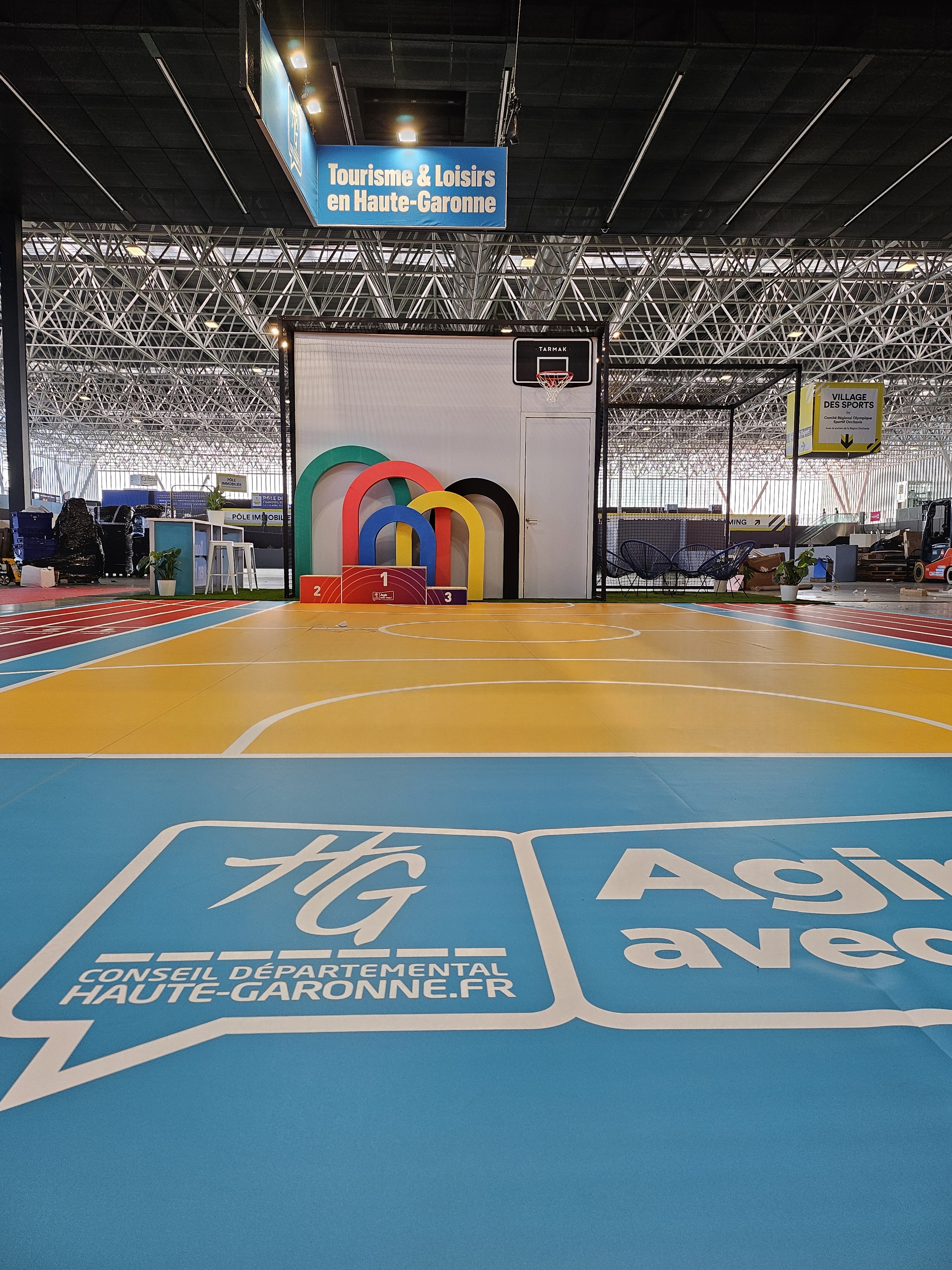 Sol avec le logo du département de la Haute-Garonne et sol d'un terrain de basket avec arches à la couleur des jeux Olympiques