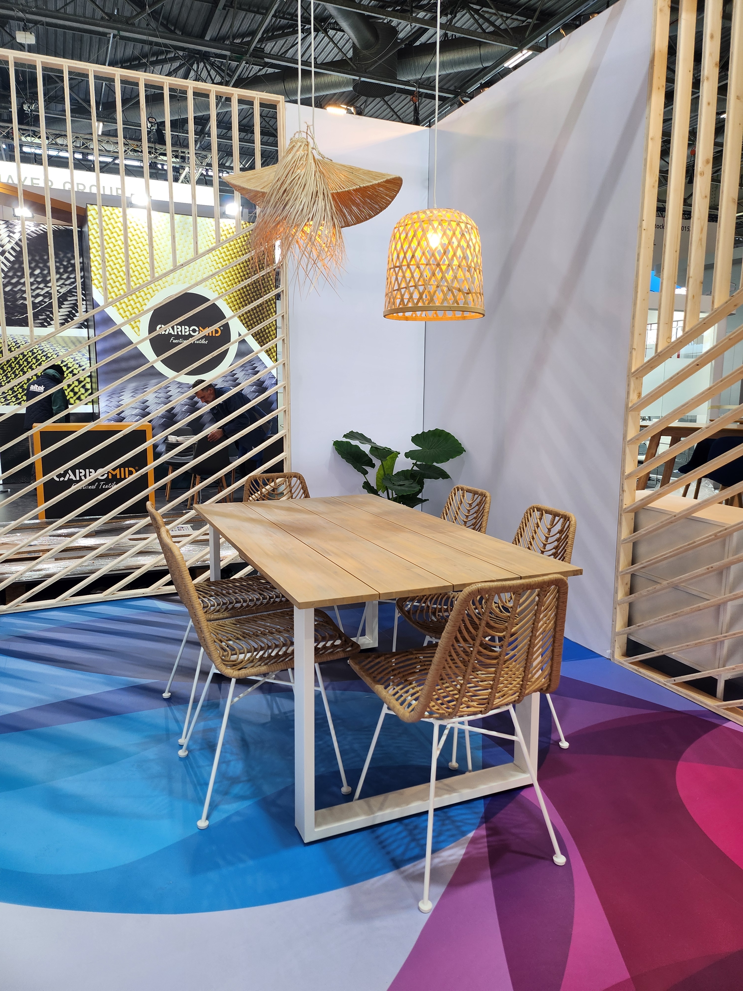 Espace d'échange sur le stand de PPG avec du mobilier en bois et des luminaires suspendus en osier