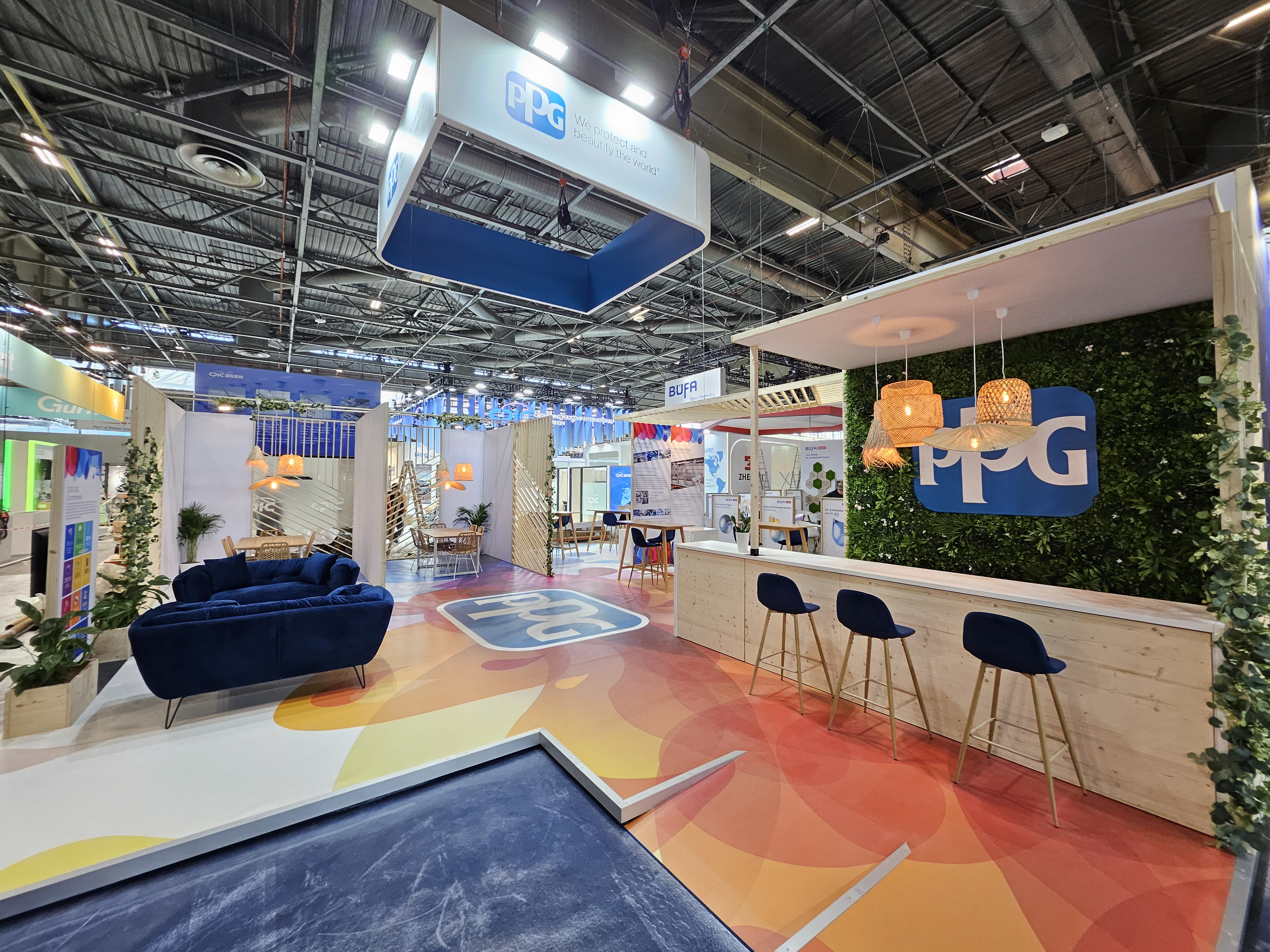 Stand de PPG au salon JEC World 2025, avec un sol personnalisé, enseigne haute, deux canapés en velours bleu et un espace d'échange